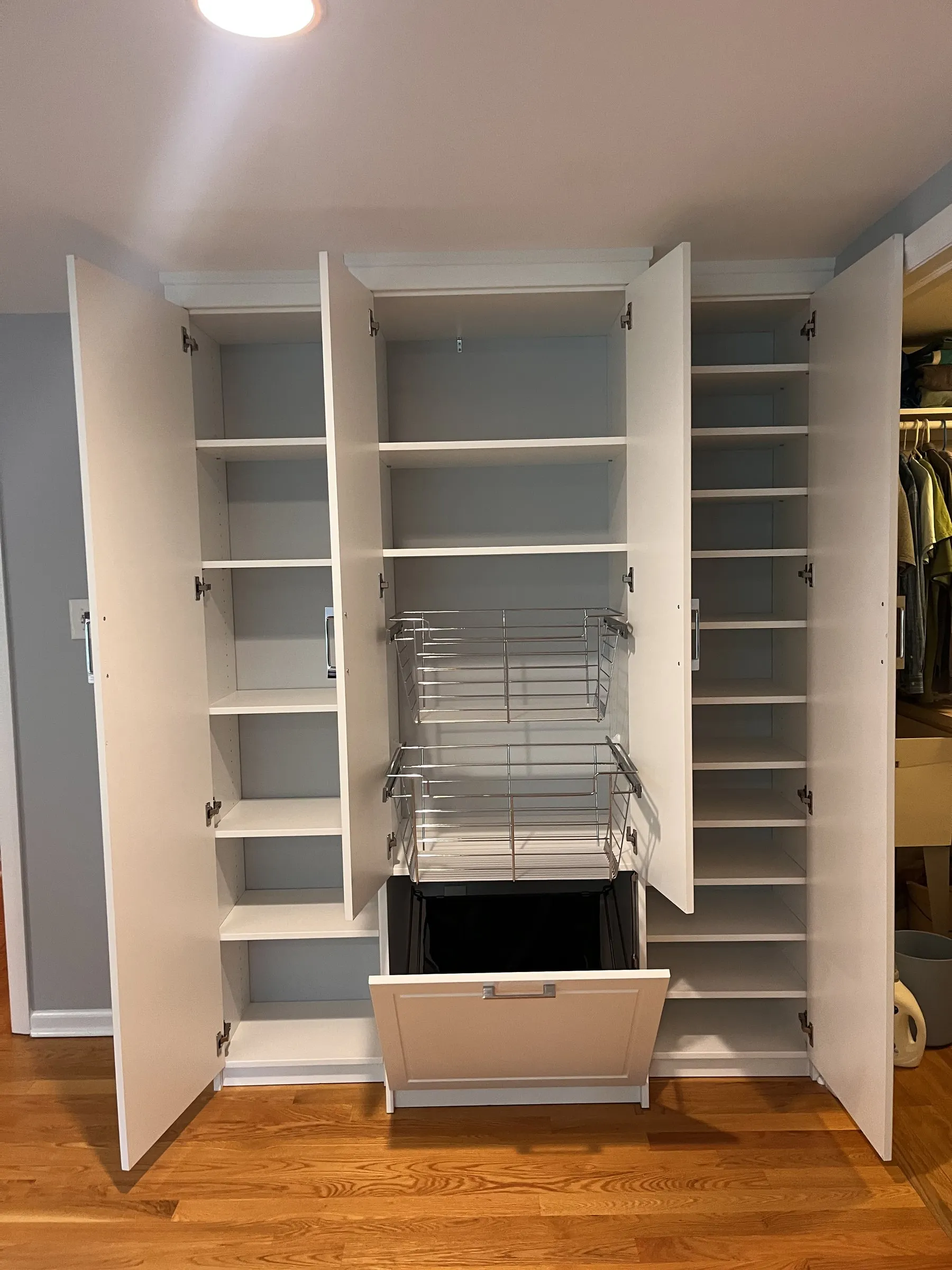 White built-in cabinet with a pull-out wire basket and a tilt-out hamper