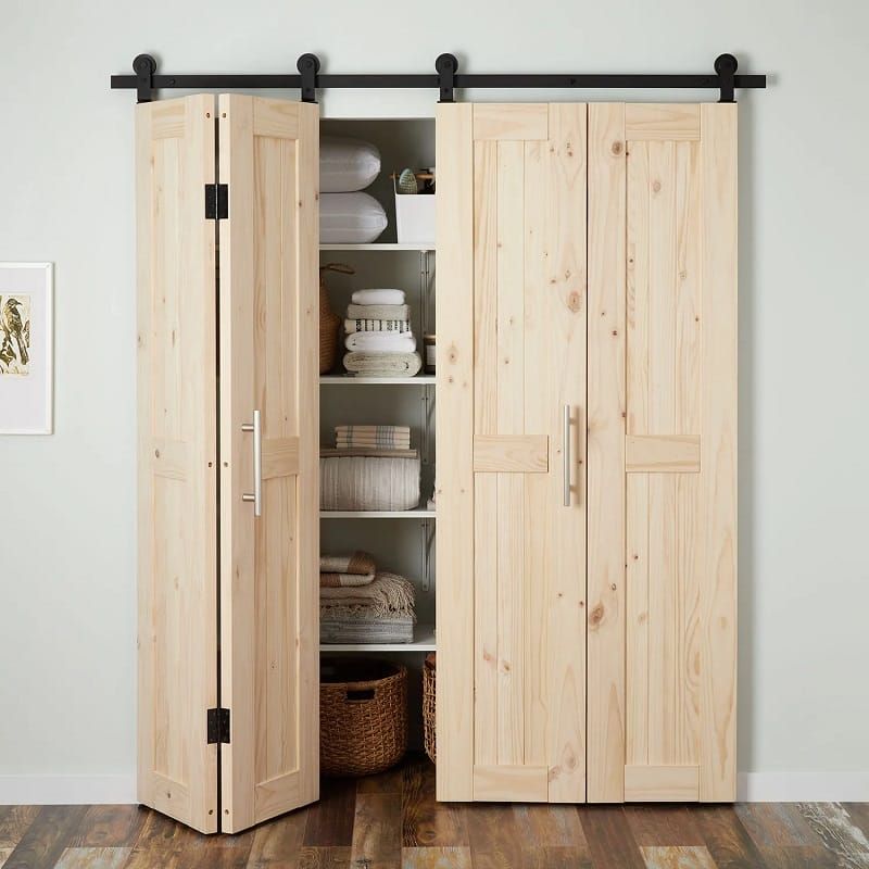 Light wood storage cabinet with sliding barn-door hardware; one door is open to reveal shelves with dishes, linens, and baskets.