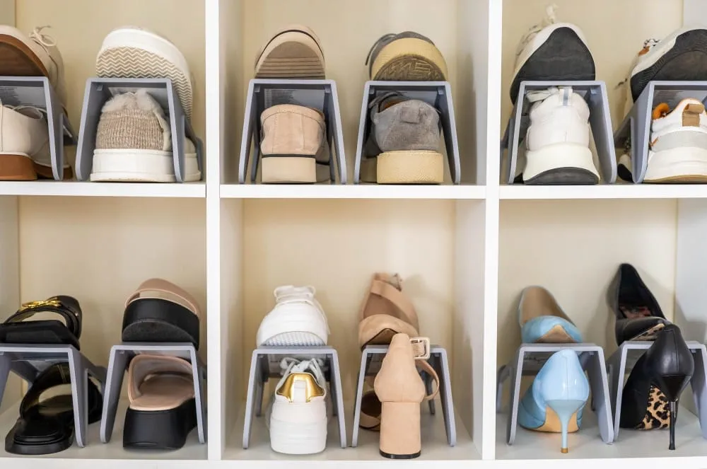 Organized closet shoe storage with cubby shelves and gray stackable shoe organizers holding sneakers, flats, heels, and boots.