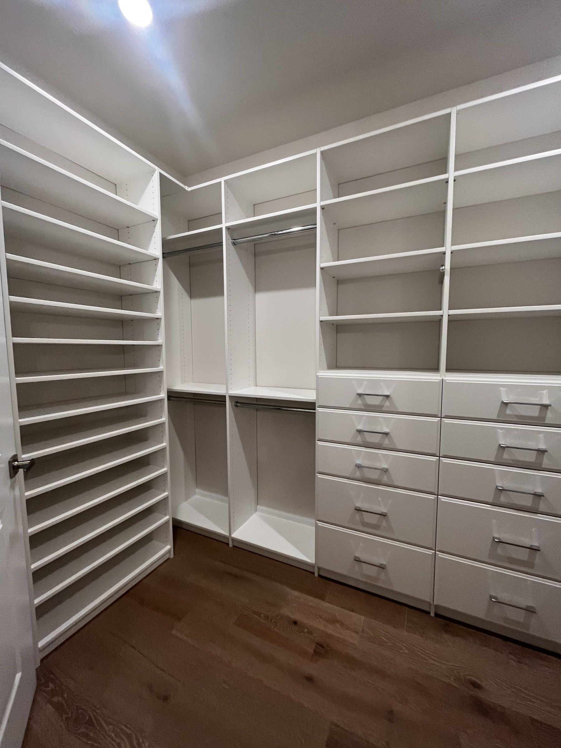 White walk-in closet with an angled shoe wall and drawer bank