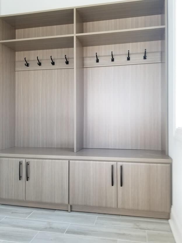 light colored gray mudroom storage unit with black hooks and lower cabinets