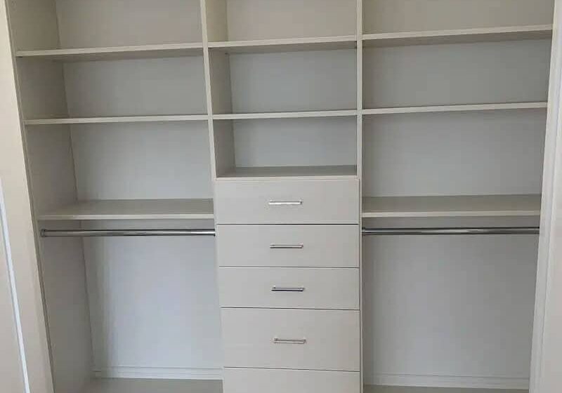 A neatly organized closet with white shelving units, drawers, and hanging rods, providing ample storage space.