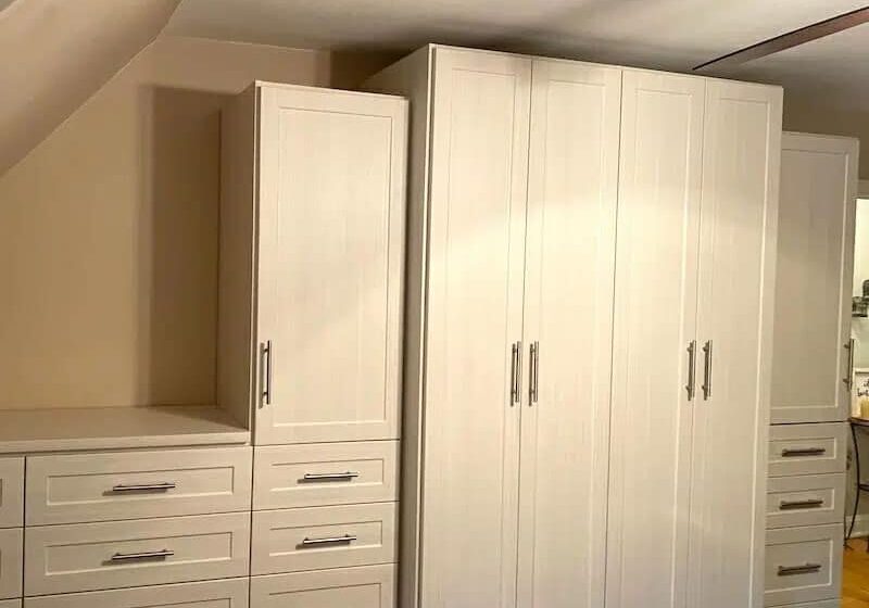 A modern wardrobe setup with beige cabinets and drawers, featuring sleek handles, in a room with a ceiling fan.