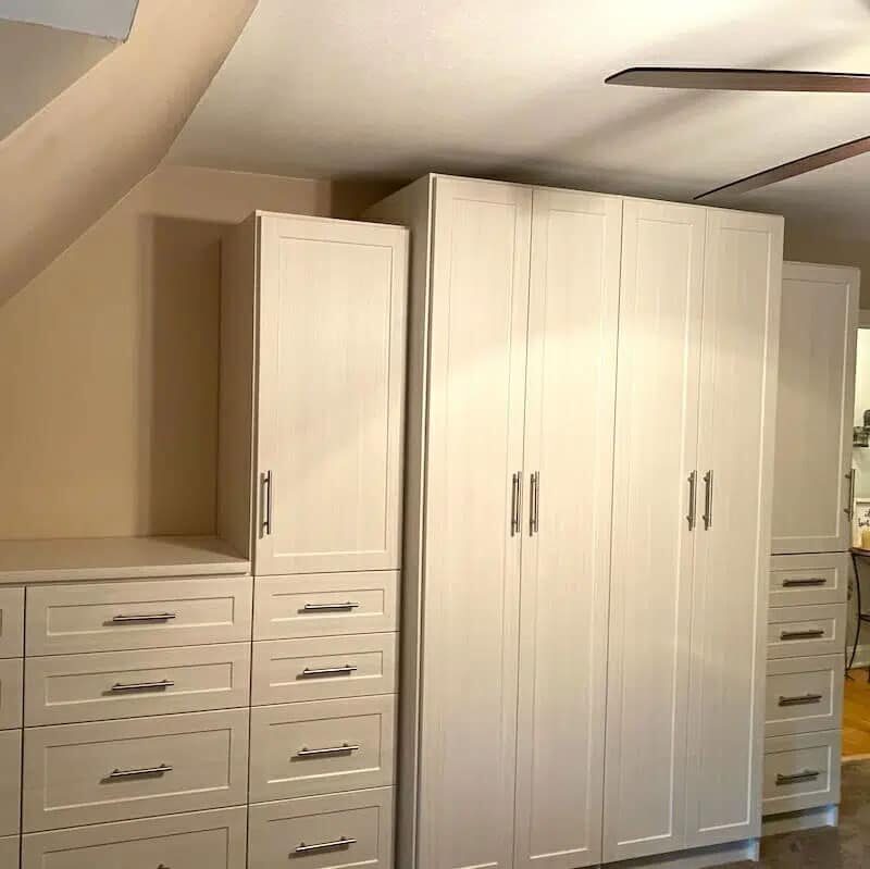 A modern wardrobe setup with beige cabinets and drawers, featuring sleek handles, in a room with a ceiling fan.